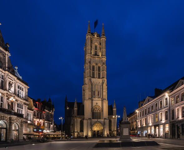 De verlichte toren van de Sint-Baafskathedraal bij het vallen van de avond