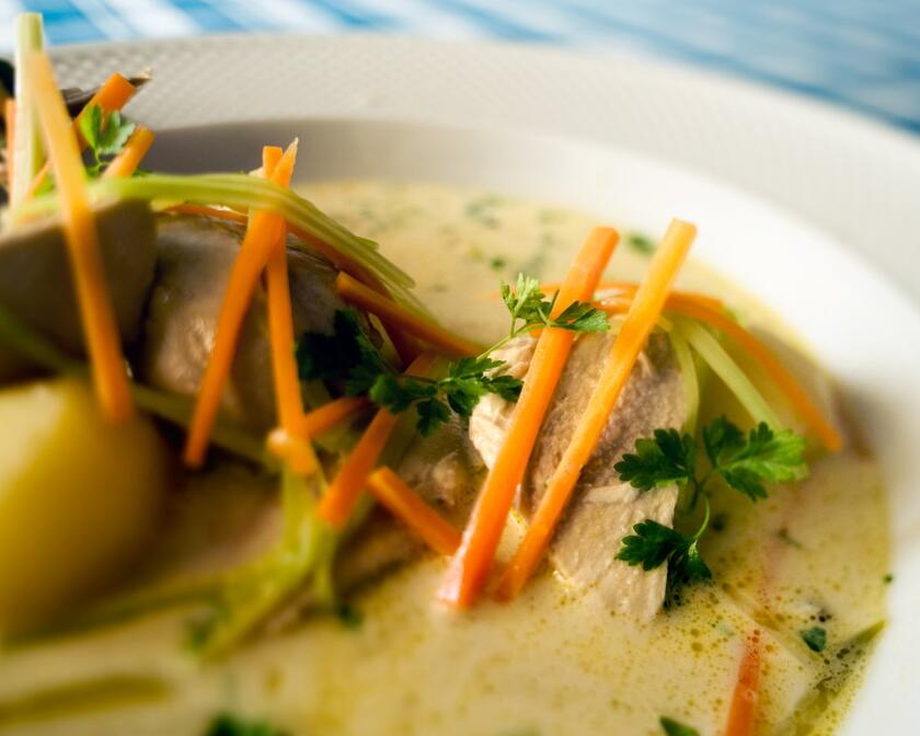 Un plato de Gentse waterzooi: patatas y pollo en un plato con sopa de verduras. Se ven zanahorias, puerros y cebollas, terminados con perejil rizado.