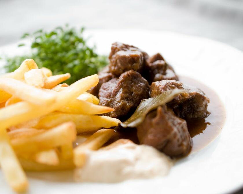 Une assiette blanche avec des frites belges et un ragoût : du bœuf dans une sauce brune. La salade est du cresson.