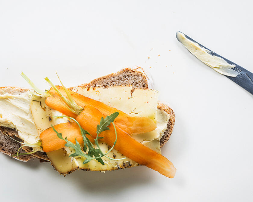 enkele sneden brood met boter, kaas, wortel en rucola, een mes met boter aan