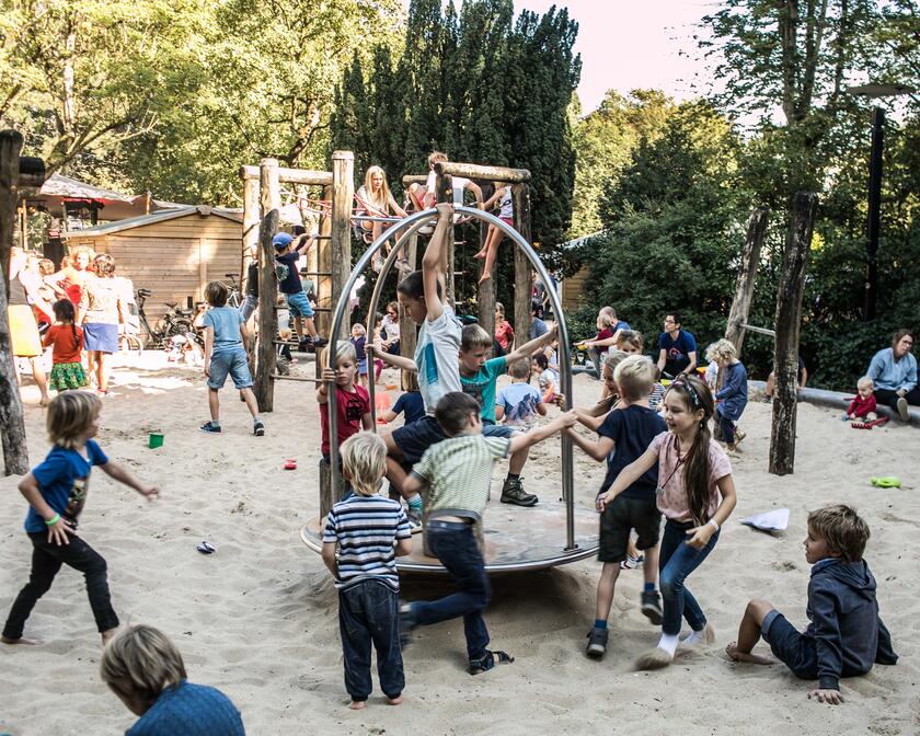 Many children are playing on a playground in the sand. It's a sunny day.