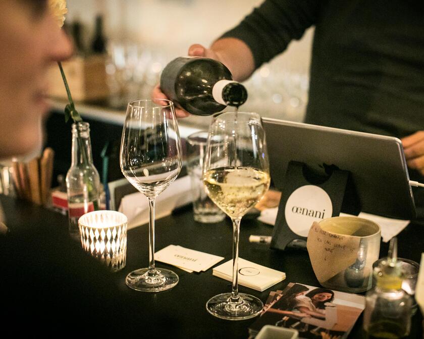 Barman pours white wine into two glasses.