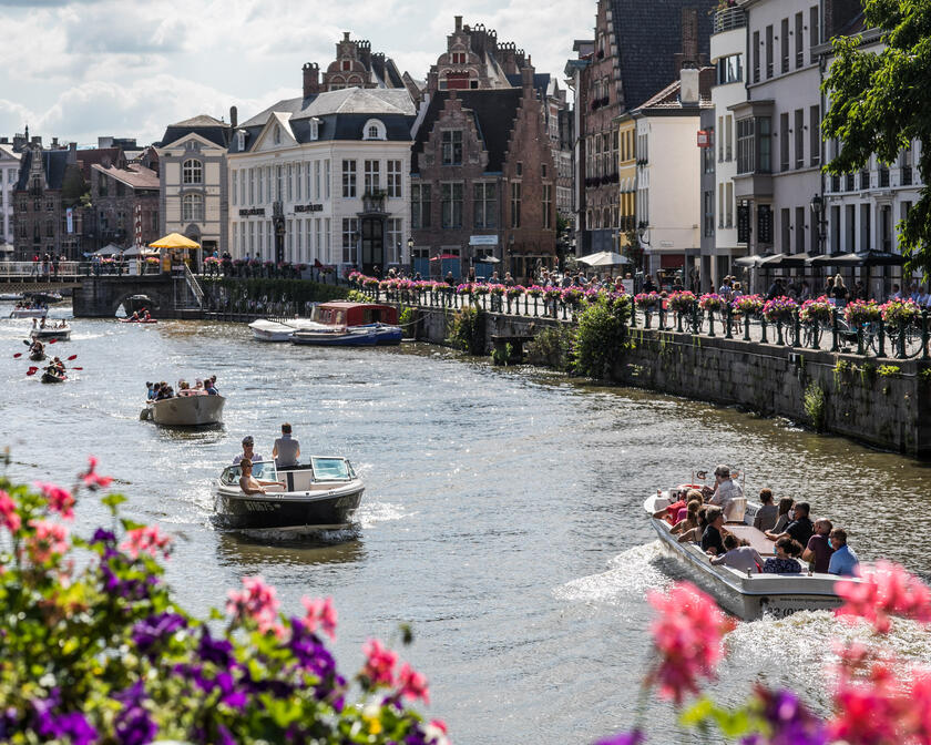 Gent, de Leie, op een zomerse dag. Er zijn plezierbootjes, gegidste boottours en kajaks aanwezig op het water.