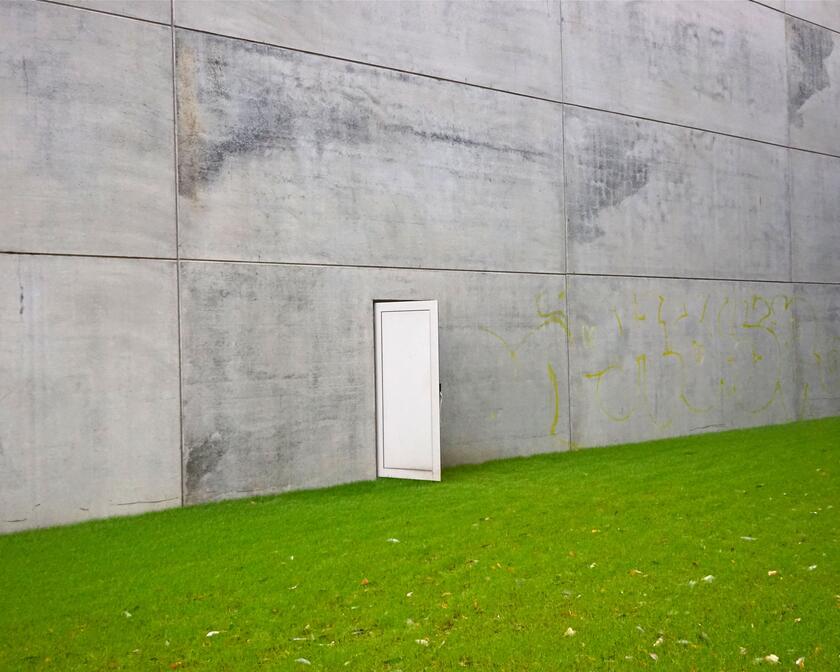 grasveld met een betonnen muur waar een witte deur op een kier staat