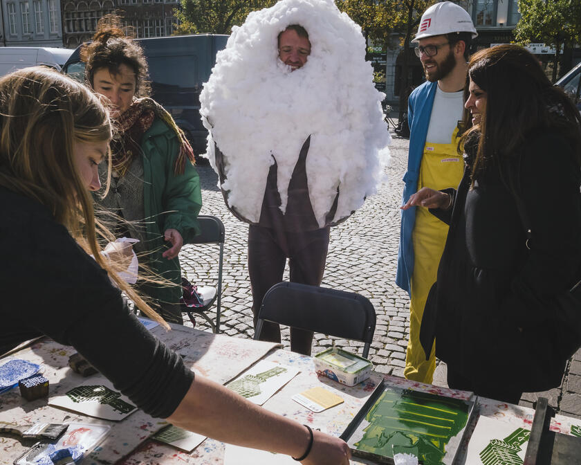een groep mensen aan een tafel buiten, een man die een kostuum van witte wol aanheeft