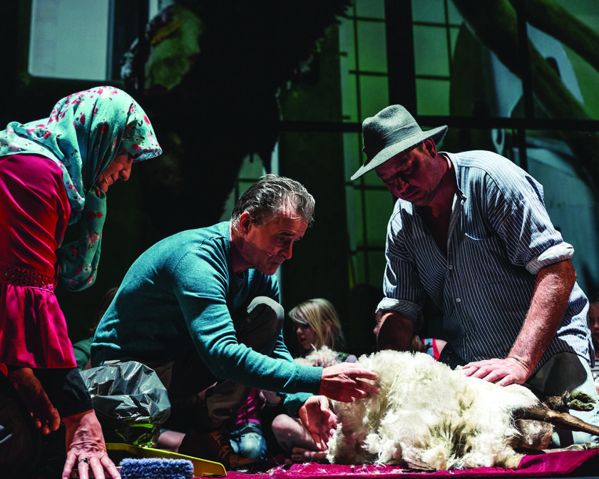 Twee mannen en een vrouw zitten op scène rond een schaap