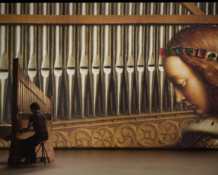 iemand die op een orgel aan het spelen is, een grote foto van een tafereel van het lam gods waarbij een engel op een orgel speelt