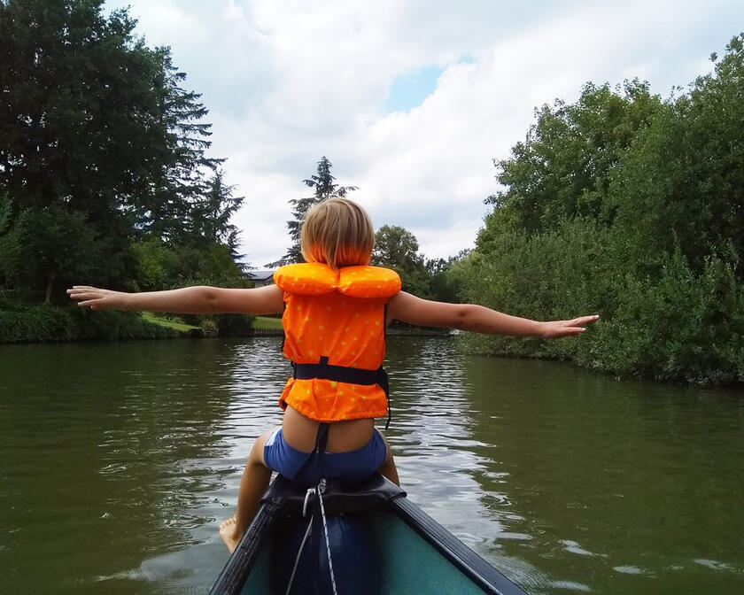 kindje met reddingsvest dat op de punt van een kano zit op de rivier tussen het groen