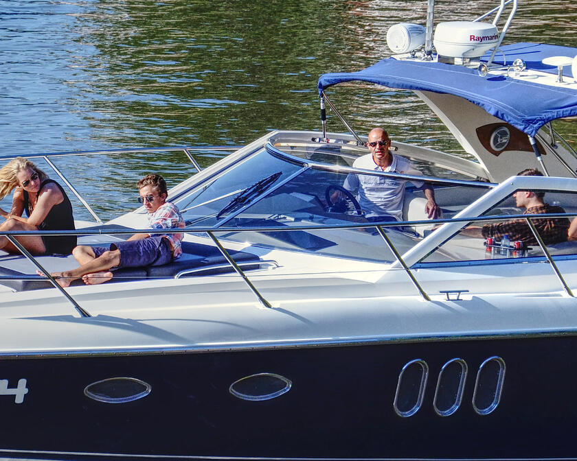 5 summerly dressed people enjoying a boat trip in a small yacht