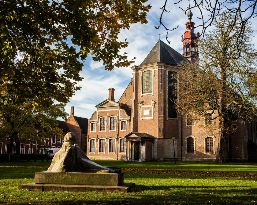 Sint-Elisabethkerk in het Oud Begijnhof, met grasplein, standbeeld van Georges Minne en herfstbomen op de voorgrond.