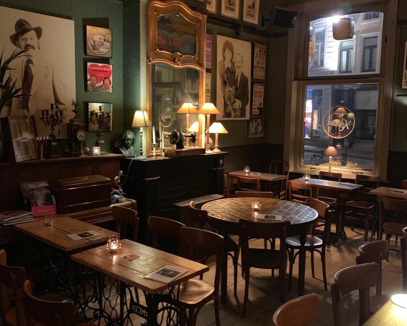 binnenkant café romain met houten tafels en stoelen, de muren hangen vol met oude foto's, een spiegel