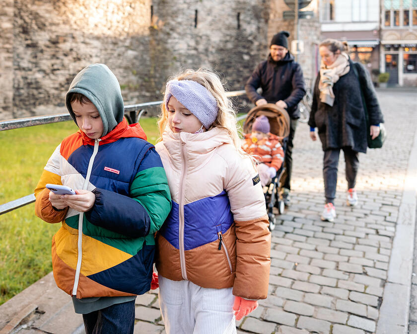 Twee kleurrijk geklede kinderen volgen de draakje Fosfor route op een smartphone