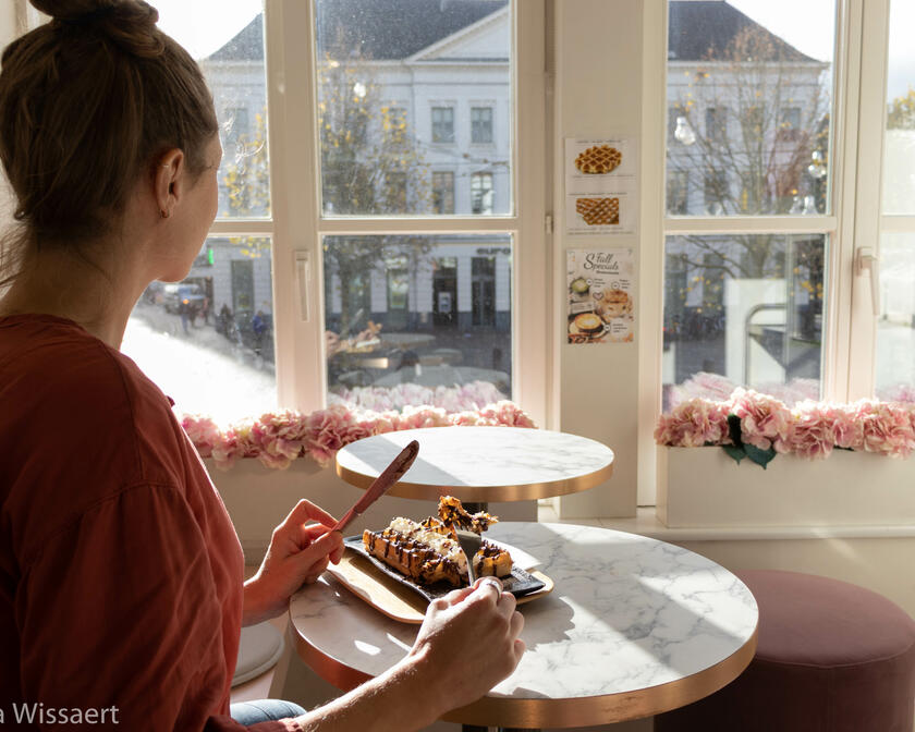 Une femme mange une gaufre avec vue sur le Groentenmarkt
