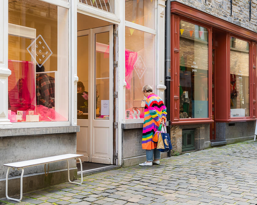 Vrouw met kleurrijke streepjestrui kijkt in etalage van winkel in de Serpentstraat in Gent