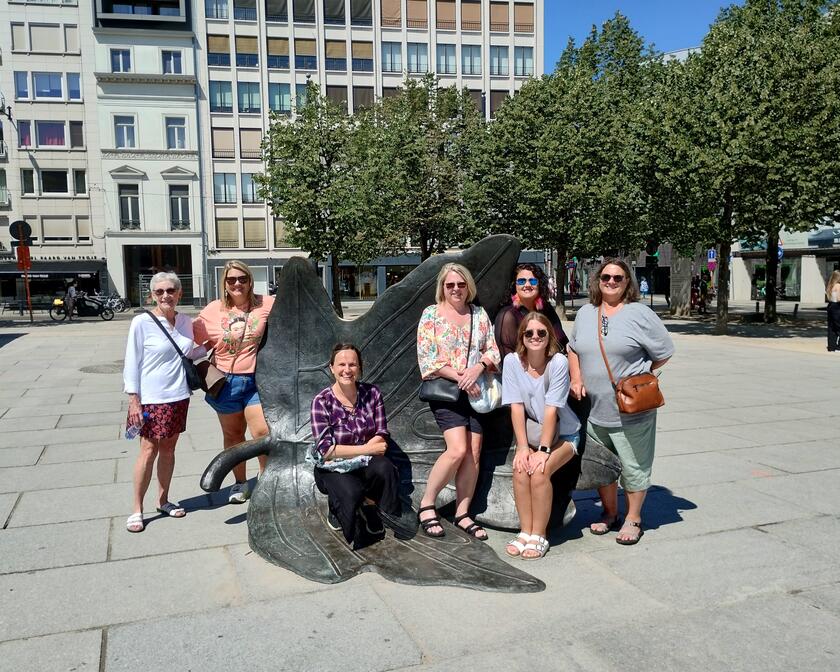7 vrouwen poseren bij een metalen beeld van een boomblad