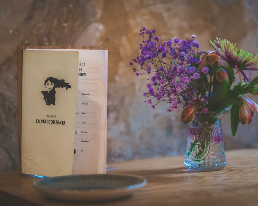 ©La Malcontenta Menu card next to a vase of purple flowers on a wooden table