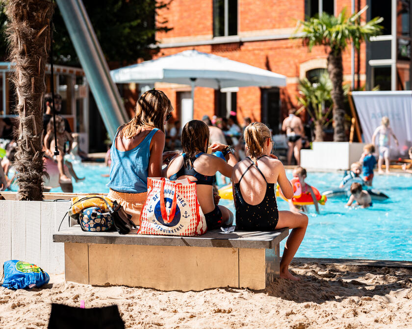 3 mensen zitten op een bankje in het zand