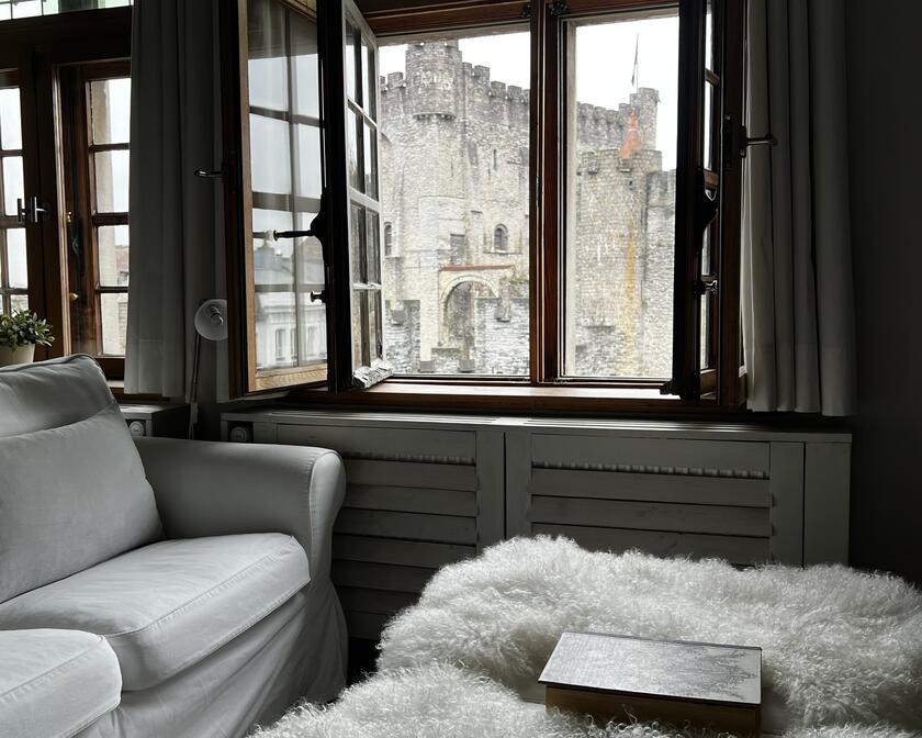 Vue par la fenêtre d’une chambre de B&B donnant sur un château gris à Gand.