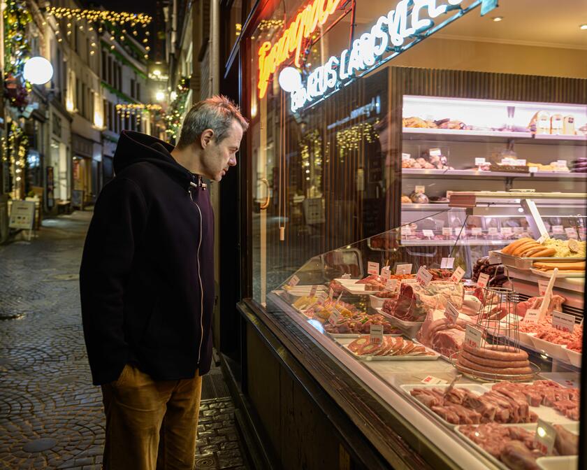 Sterrenchef Olly Ceulenaere kijkt naar vlees in verlichte vitrine van Gentse beenhouwerij bij het vallen van de avond