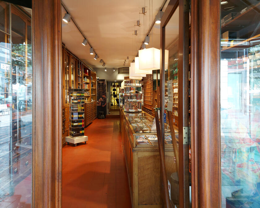 Deuropening van de winkel, met links en rechts klassieke houten kasten en toonbanken waarin pennen, notaboekjes en scheerartikelen liggen. De winkel heeft een rode vloer