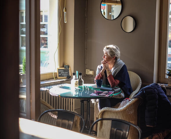 Vrouw zit aan een tafeltje in een sandwichbar met rotan zetels.