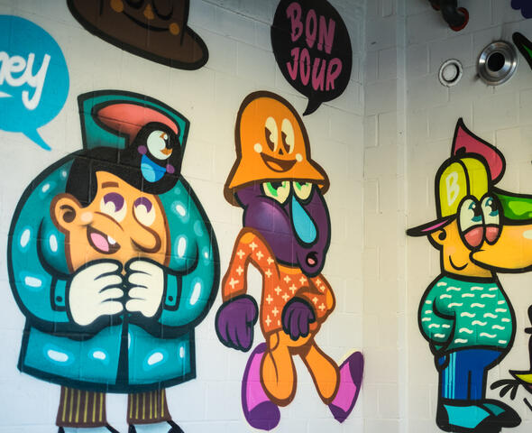 Kleurrijke animatiefiguren op een witte muur met graffiti.