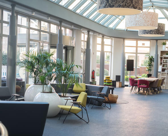 Ruime open inkomhal met zitplaatsen, leeshoek, grote plantenvazen.