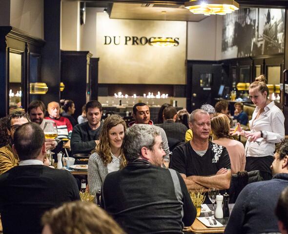 Binnenzicht met dicht opeengepakte houten tafels, zwarte muren met oude foto's van Gent.