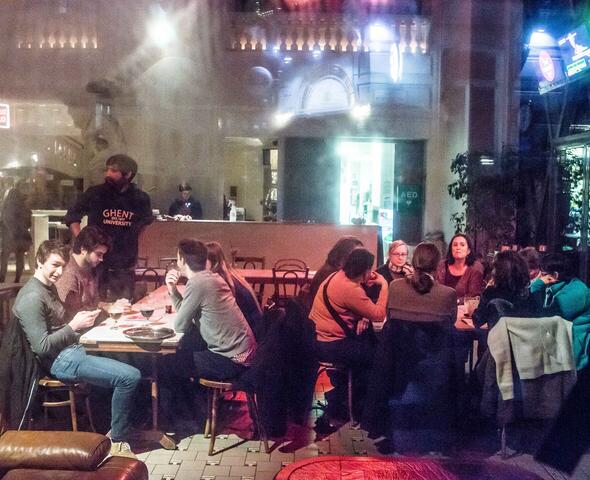 Mensen die in het Vooruit café aan tafels zitten, een lange bar met iemand achter.