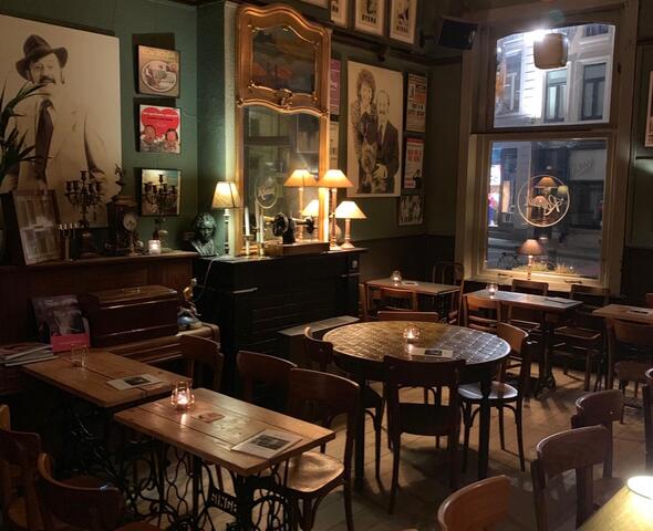 binnenkant café romain met houten tafels en stoelen, de muren hangen vol met oude foto's, een spiegel