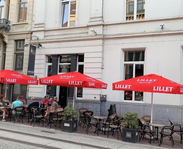 rode parasols voor een restaurant met tafels en stoelen eronder, mensen aan de tafeltjes