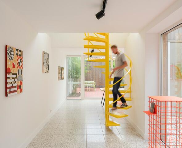 witte kamer met een gele draaitrap, een oranje rekje, schilderijen aan de muur