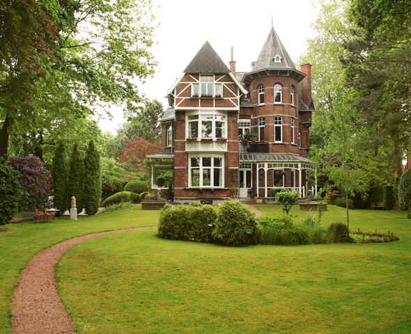 The Villa in the centre of the garden with the path to the villa in the foreground and the pond surrounded by plants