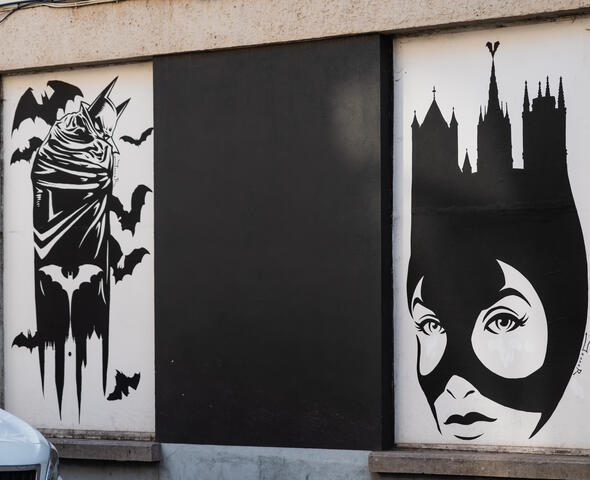 Dibujo mural en blanco y negro de una figura inspirada en Batman con las Tres Torres de Gante
