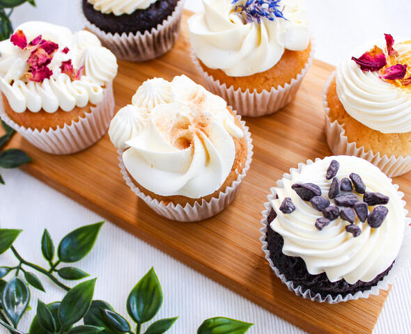 6 cupcakes met witte crème en bloemen op een houte plank
