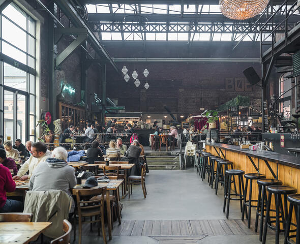 Foodhal in industrieel gebouw met tal van tafeltjes vol gasten