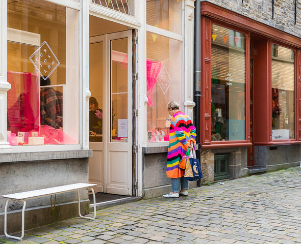 Vrouw met kleurrijke streepjestrui kijkt in etalage van winkel in de Serpentstraat in Gent