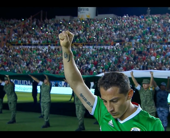 Een voetballer met opgeheven hand en een menigte die minutenlang stilte houden