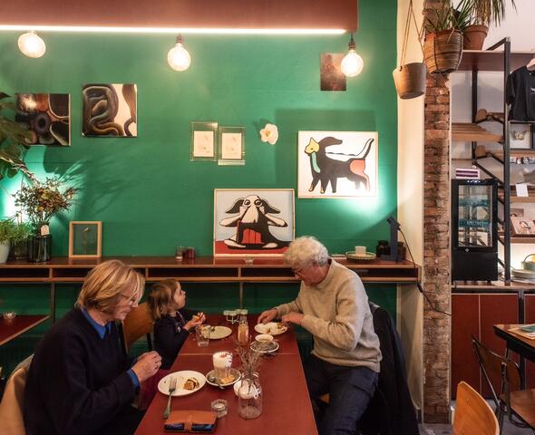 Twee volwassenen en een kind zitten aan een tafel koffie te drinken