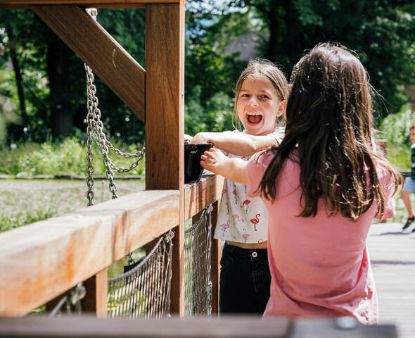 Two girls are standing by a wooden structure in the museum garden, having fun.