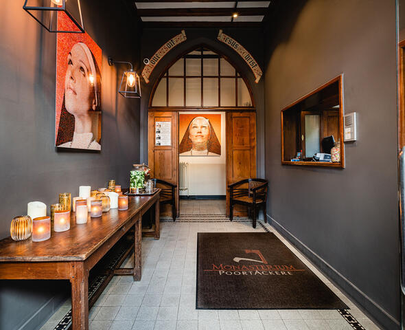 inkomhal met houten accenten. Langs de linkerzijde staat een houten tafel met kaarsen. Aan het einde van de gang is er een verlicht portret