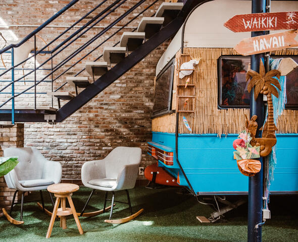 Twee stoelen op kunstgras staan links van een blauw-witte caravan