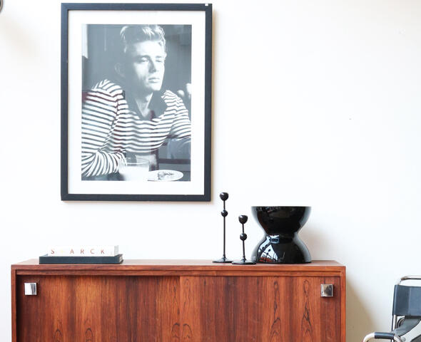 Een stijlvol mid-century dressoir van warm hout, gedecoreerd met vintage objecten en een bijpassende fotokader aan de muur
