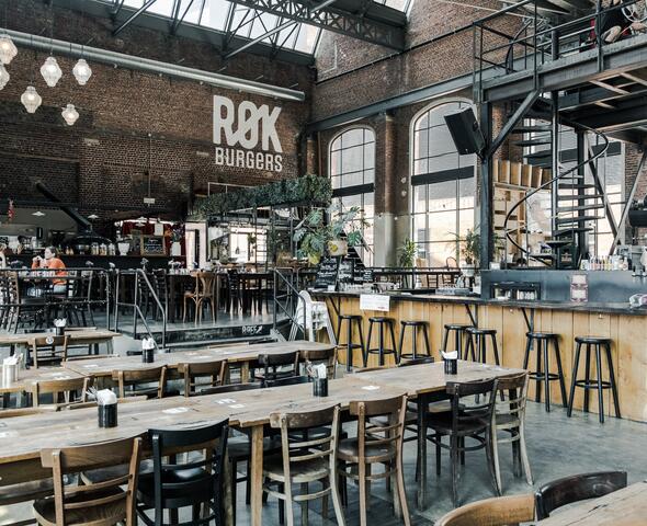 A large hall with tables and chairs, a bar with bar stools and a spiral staircase.