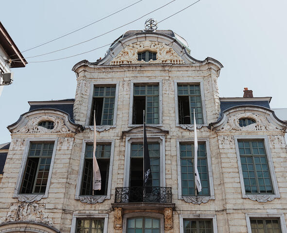 Oombergen House. A stately façade with many windows, a small wrought-iron balcony, and three flags
