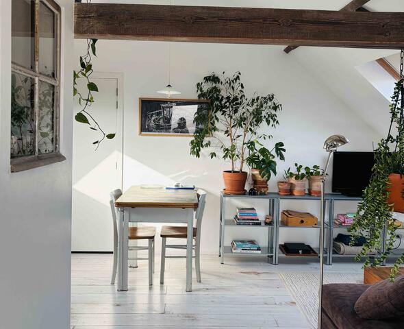 Lichtrijke zolderstudio met witte muren, houten balken, tafel met 2 stoelen en zitruimte