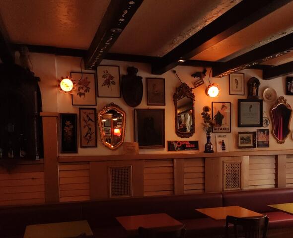 The interior of a café with a floor of black-and-white tiles. Various picture frames and rustic mirrors hang on the wall.