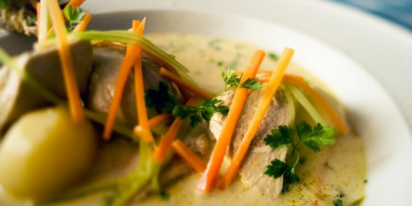 Un plato de Gentse waterzooi: patatas y pollo en un plato con sopa de verduras. Se ven zanahorias, puerros y cebollas, terminados con perejil rizado.