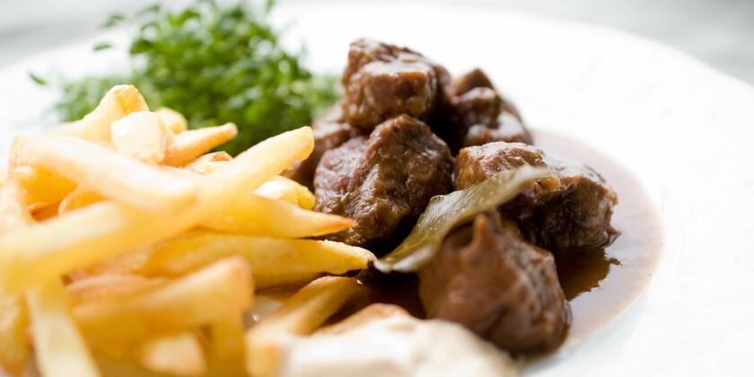 Een wit bord met Belgische frietjes en stoverij: rundsvlees in een bruine saus. Als salade zie je waterkers.