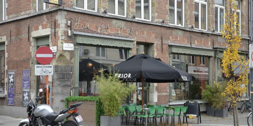 Terras van café Jan van Gent met terrastafels, groene metalen stoelen en zwarte parasols.